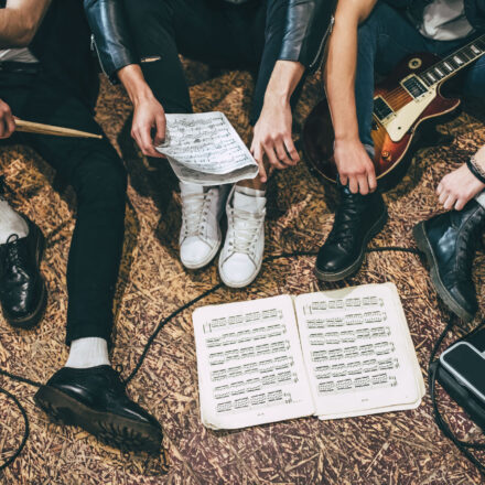 Repetition of rock music band. Cropped image of guitar players and drummer are sitting on the floor at rehearsal base with notes. Top view