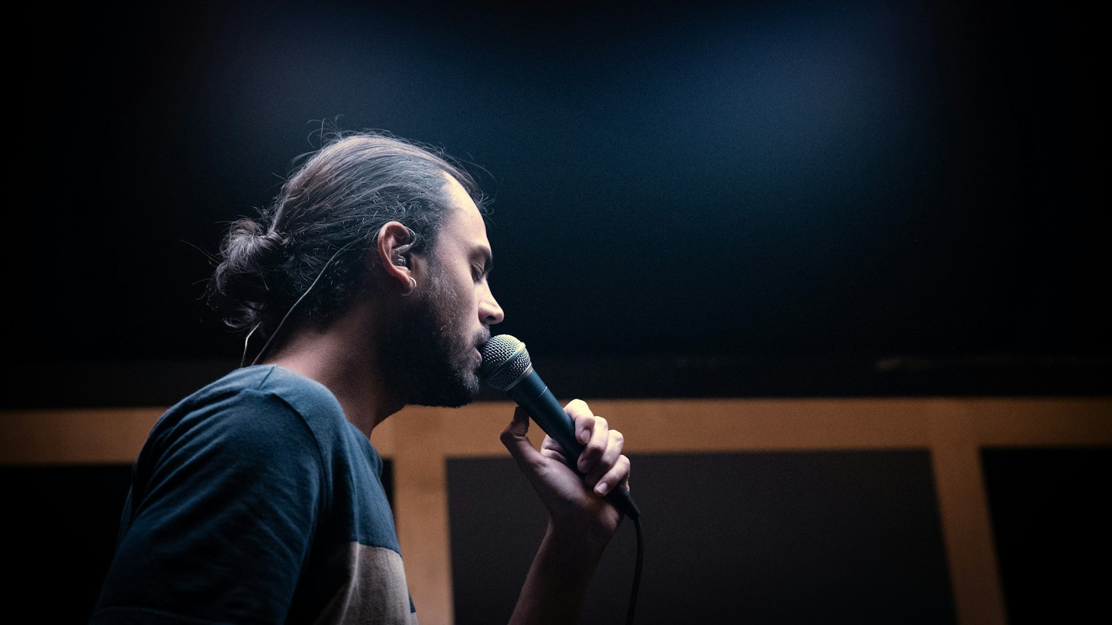 Artiste tenant un micro dans une salle de répétition sombre, avant les concerts de sortie