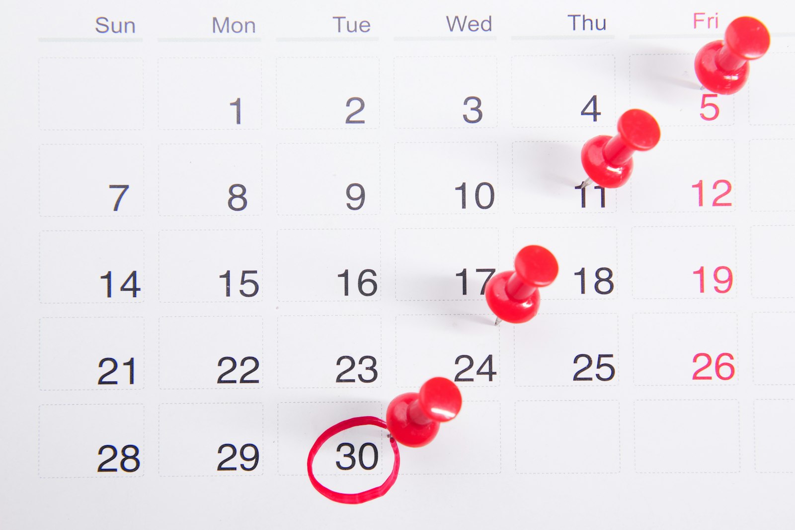 Calendrier mural avec des punaises rouges marquant des dates