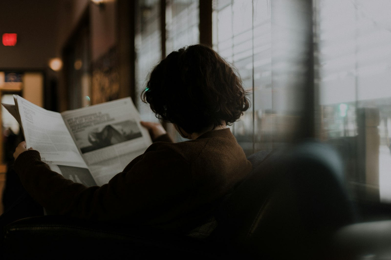 Personne lisant un magazine assise près d’une fenêtre