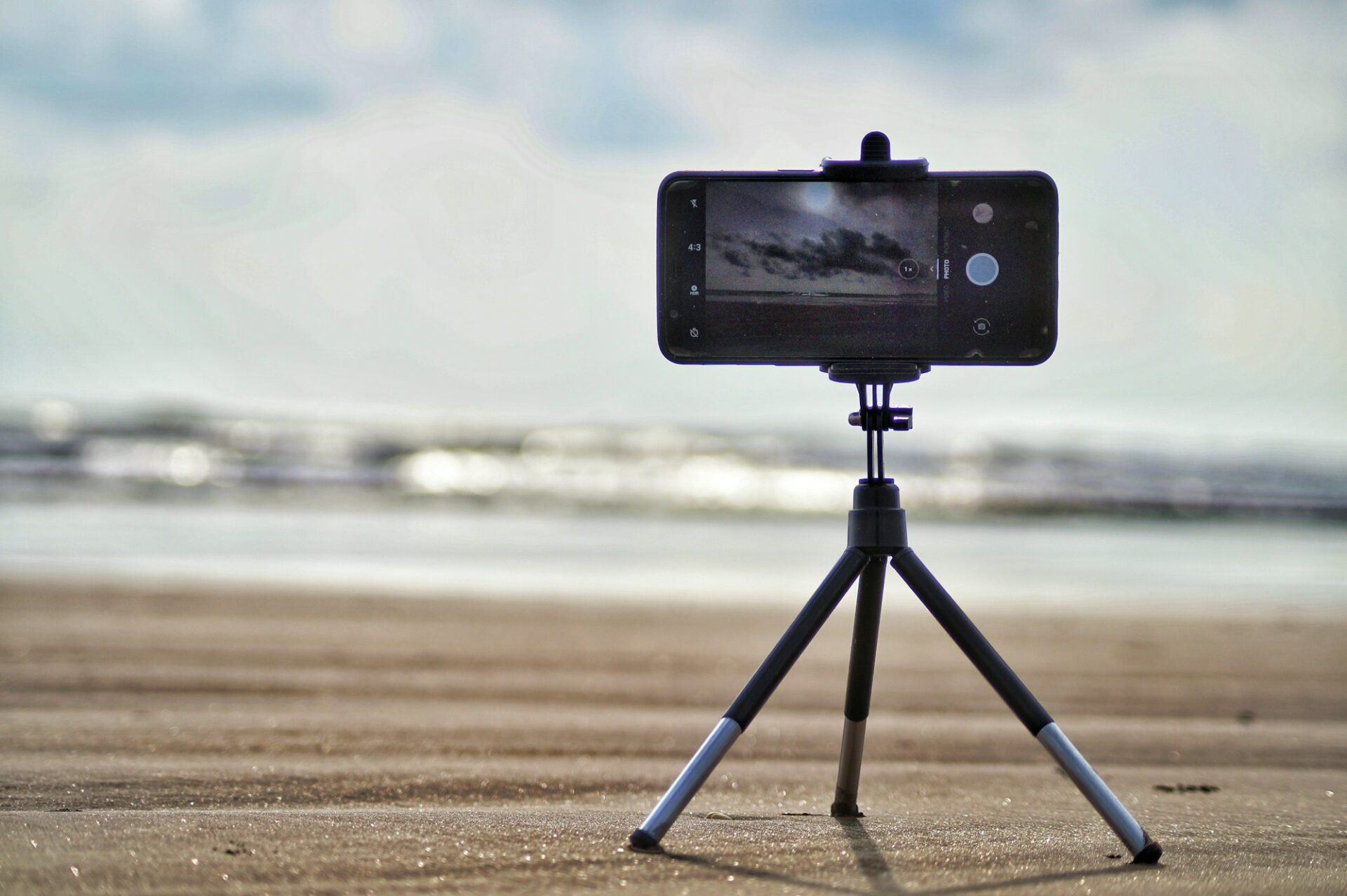 Smartphone fixé sur un petit trépied face à la mer, prêt à filmer