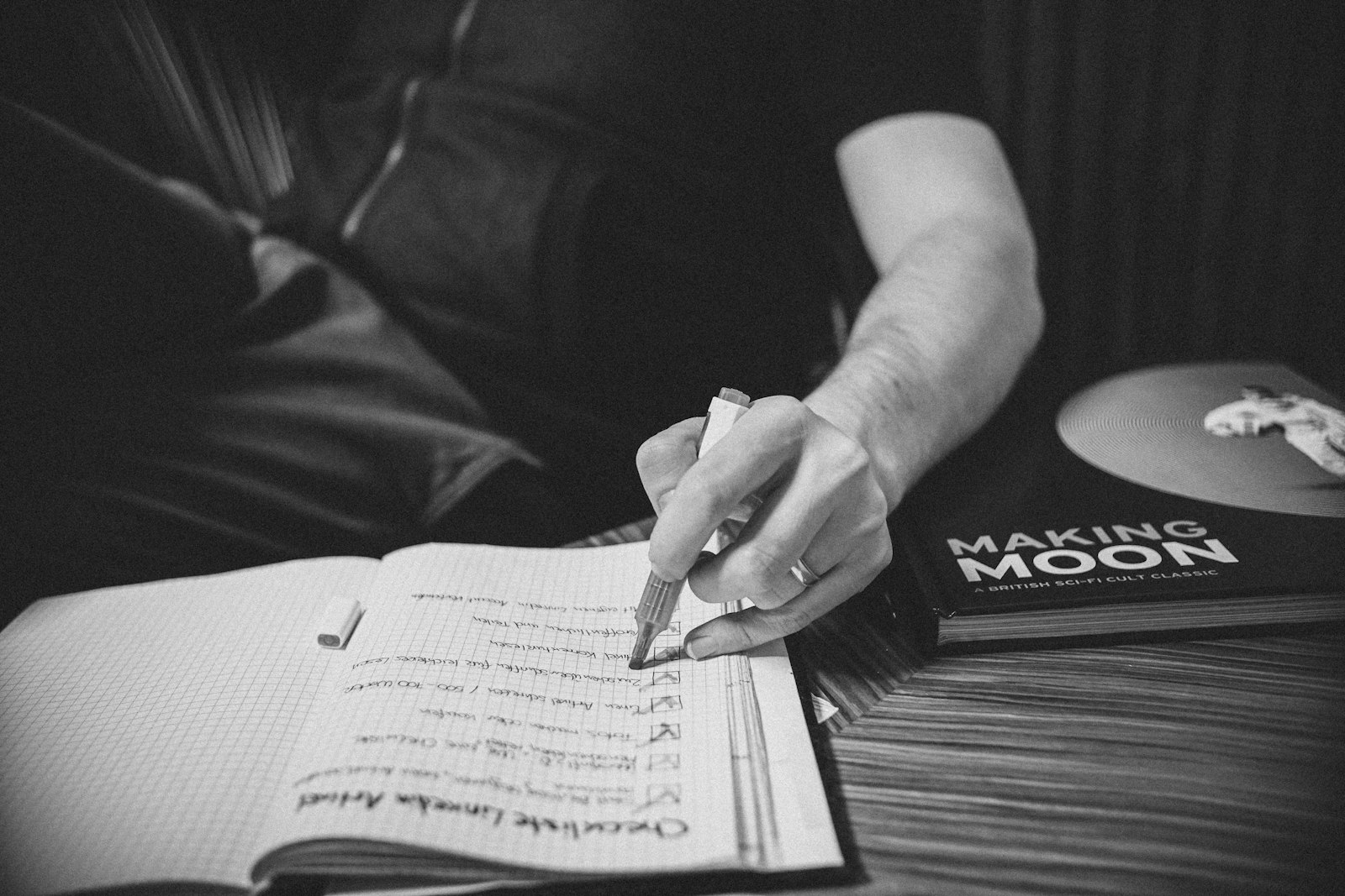 Photo en noir et blanc d’une main écrivant une liste sur une feuille