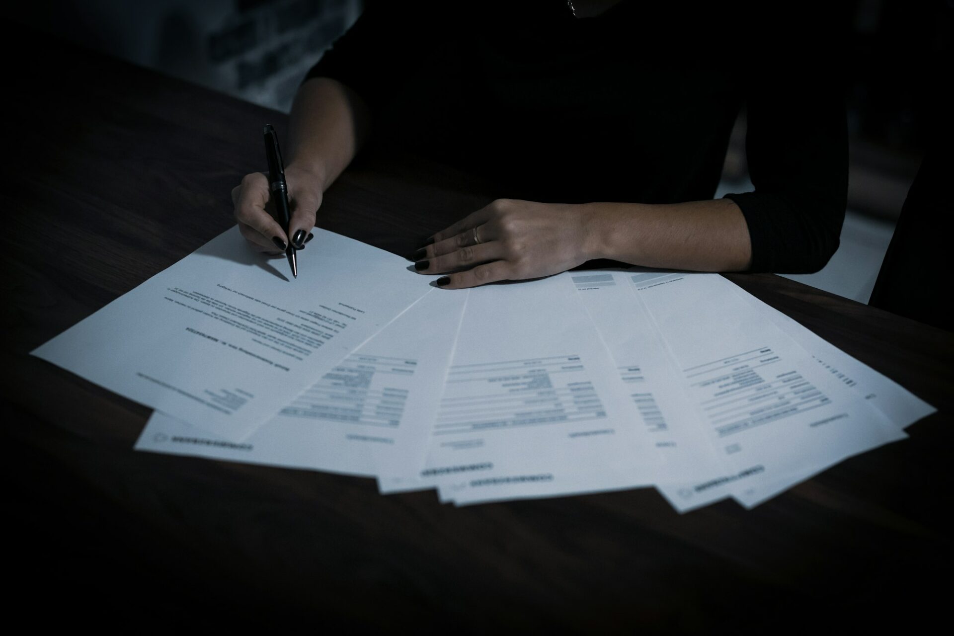 Personne signant un contrat au stylo, entourée de documents