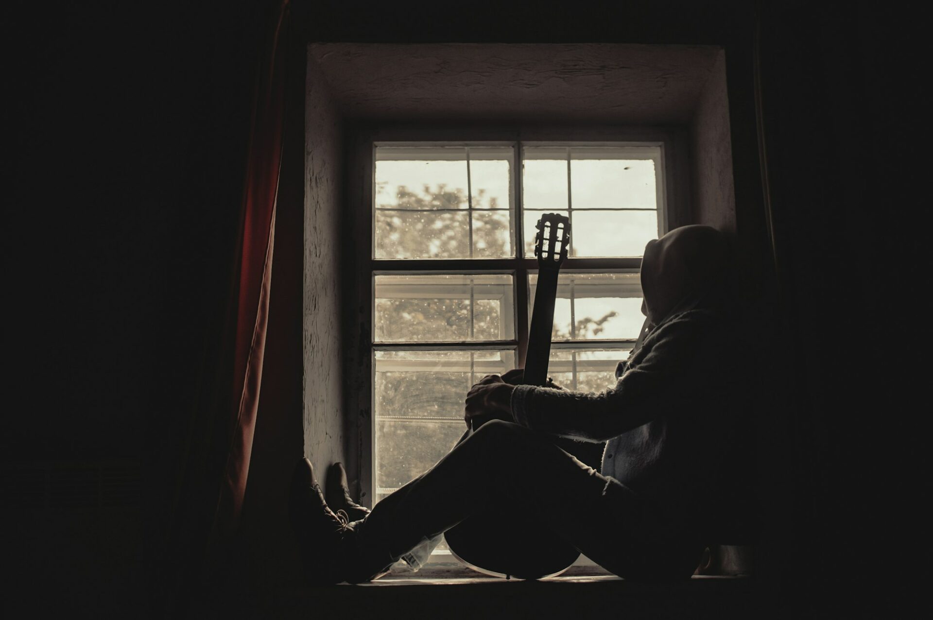 Musicien assis devant une fenêtre, sa guitare à la main, dans un moment de calme