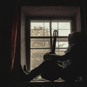 Musicien assis devant une fenêtre, sa guitare à la main, dans un moment de calme