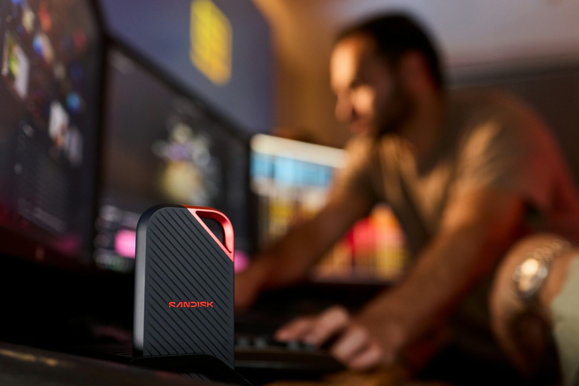 Disque SSD portable posé sur un bureau, une personne travaillant sur ordinateur en arrière-plan
