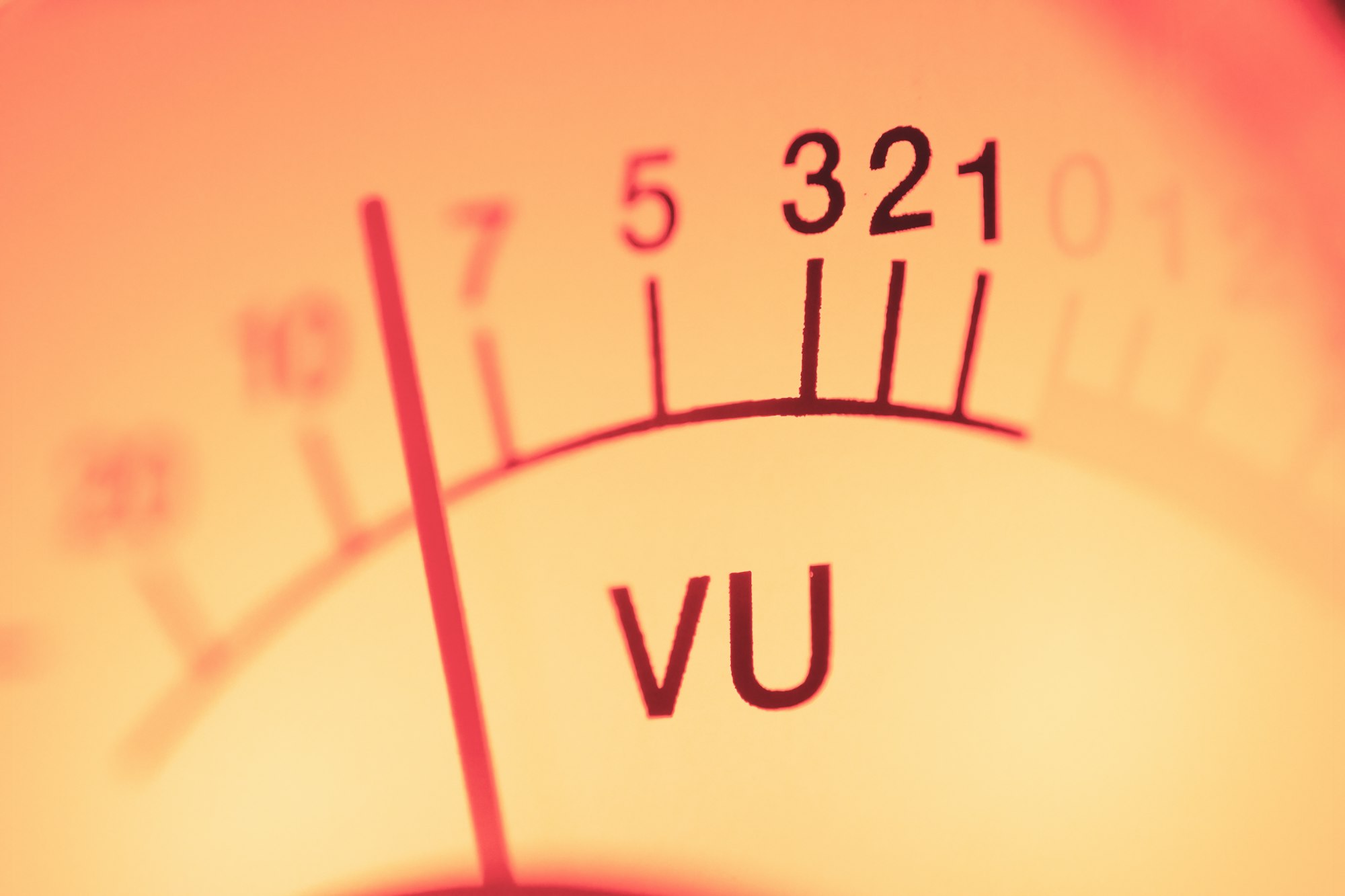 Gros plan sur un vumètre analogique à aiguille, graduations blanches et rouges