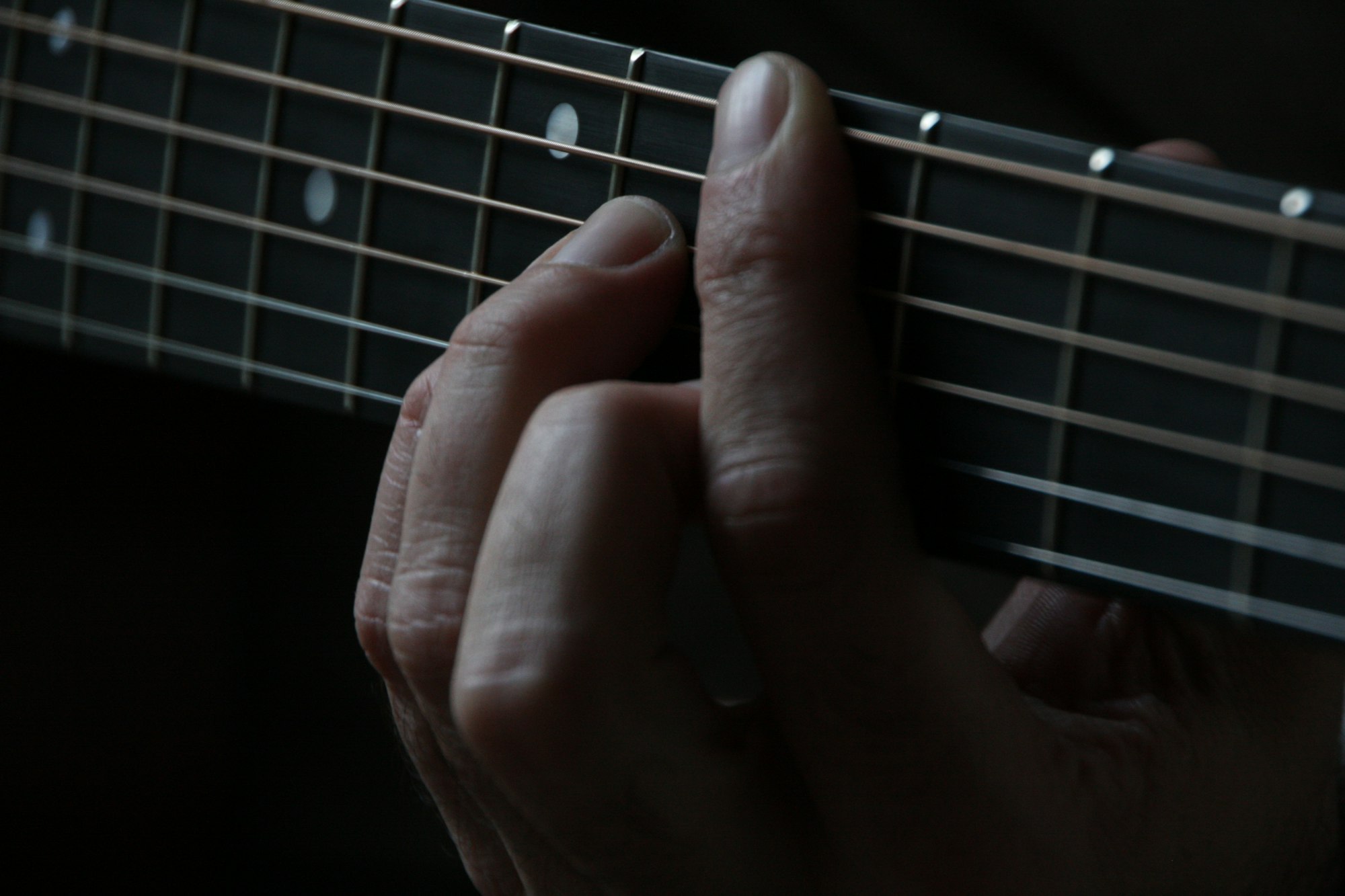 Doigts d’un musicien posés sur les frettes du manche d’un instrument à cordes