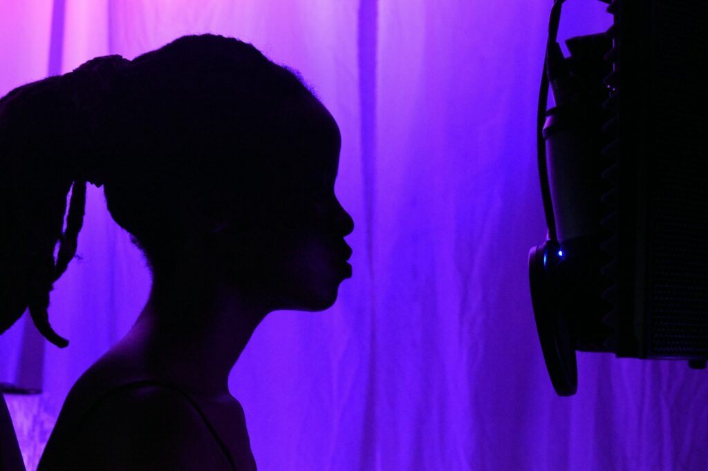 Silhouette d’une chanteuse face à un micro dans un studio éclairé de violet