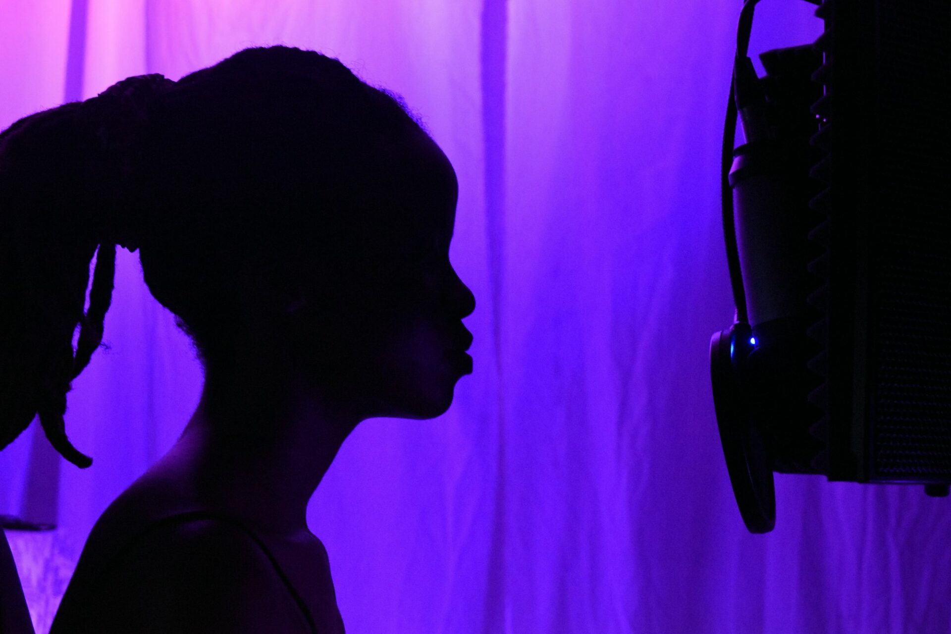 Silhouette d’une chanteuse face à un micro dans un studio éclairé de violet