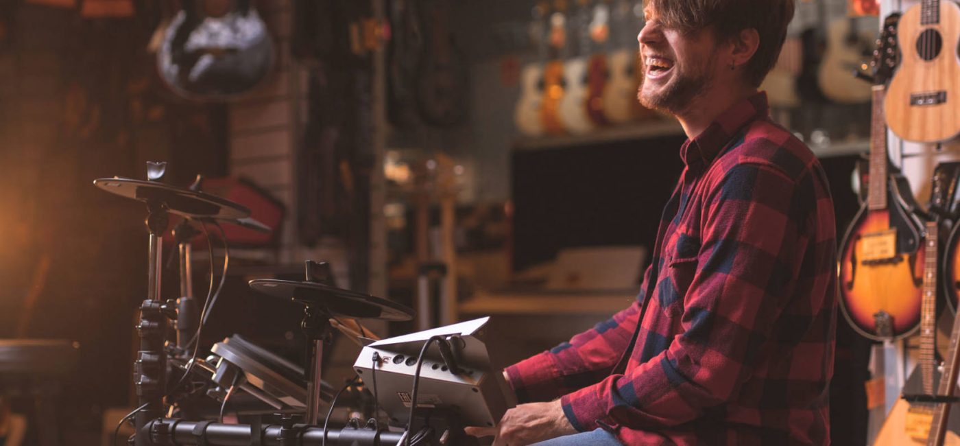 Smiling young man playing the drums in a music store